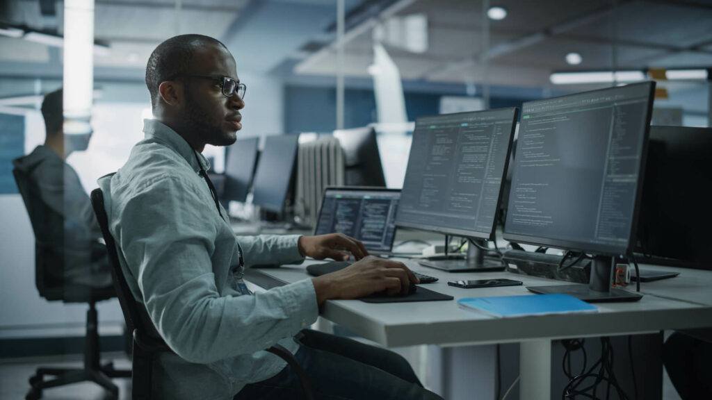 African American man typing at computer on table in front of multiple monitors