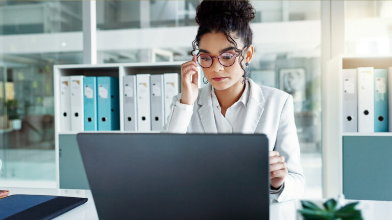 Businesswoman holding glasses in front of laptop in front of book shelves