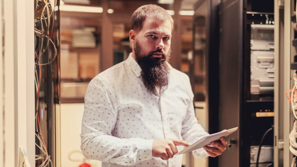 Bearded man pointing at tablet in datacenter